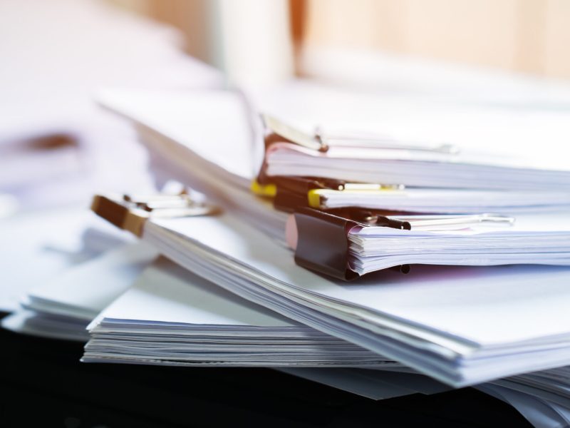 Stack of papers documents in archives files with clip papers on table at offices,  Busy offices and Pile of data unfinished folders on office desk indoor near window,  Business concept.
